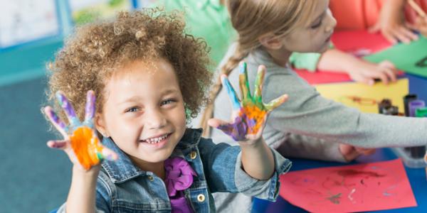 preschooler holds up hands covered in finger paint