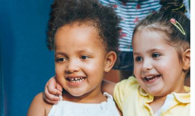 Two preschool girls sitting side by side hugging