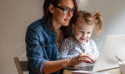 Young girl sitting her her mom's lap looking at the computer