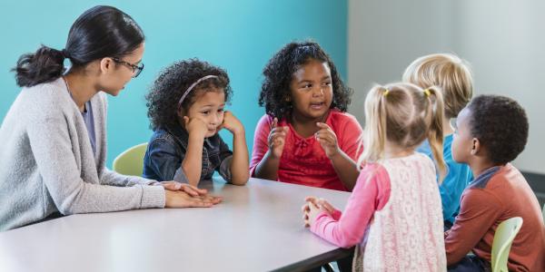 children and a teacher at a table discussing something