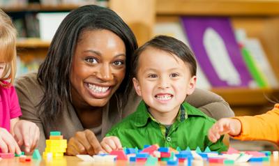 Multicultural teacher smiling with three preschool-aged students