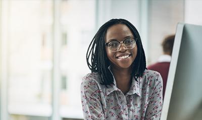 A woman behind a desktop smiles at the camera