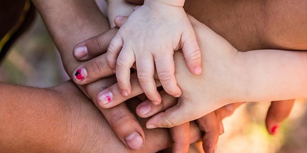 Several adults and children put their hands together