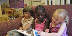 A group of children reading a book on a sofa together.