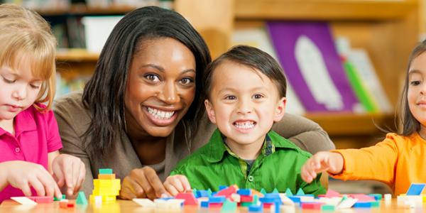 Teacher smiling with three preschoolers