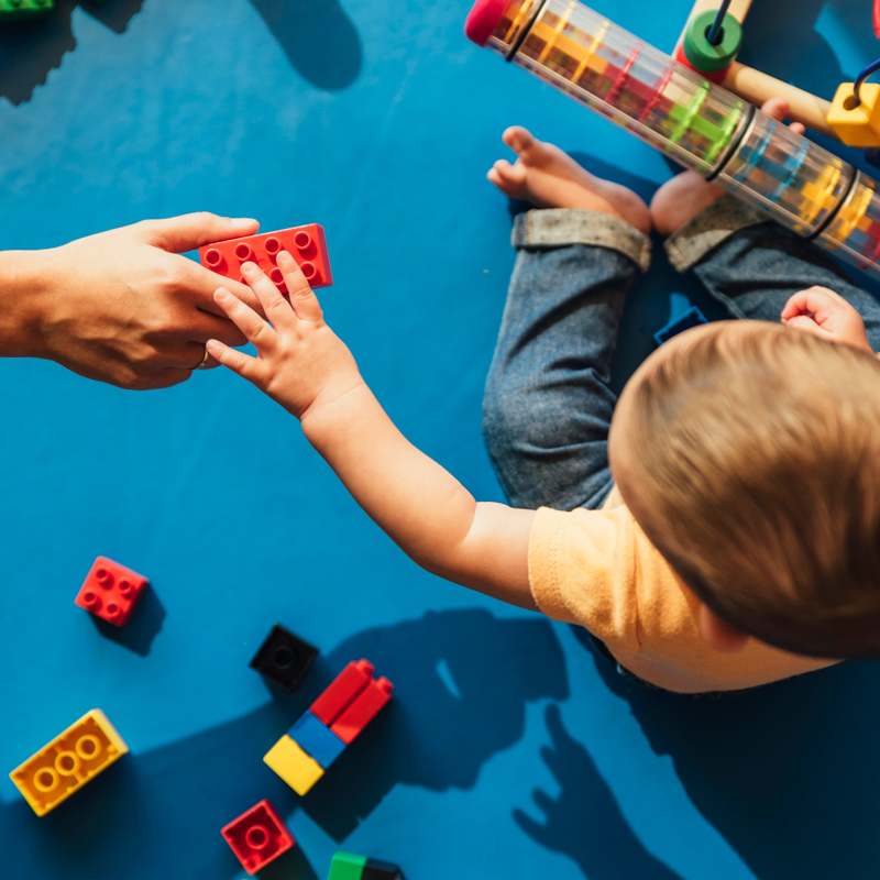 A toddler reaches for a building block from an adult