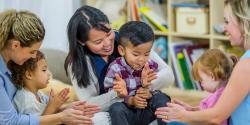 A classroom with mothers and children clapping in a circle