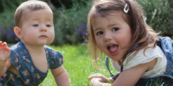 An infant and toddler laying in the grass outside