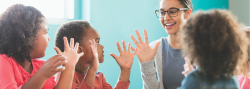 Teacher and three preschool students with hands in air